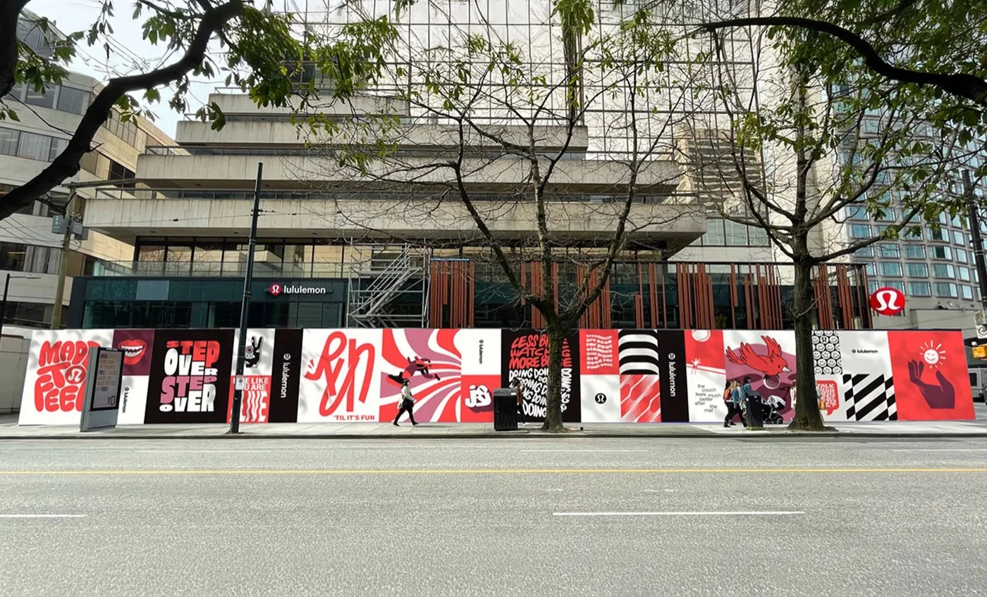 A city block wrapped in red, white and black lululemon artwork beneath a concrete-and-glass tower